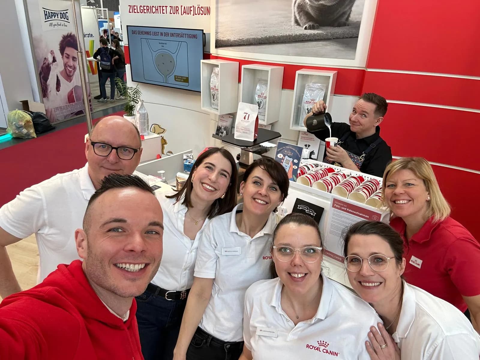 Team-Gruppenfoto an einem Messestand, im Hintergrund gießt ein Barista Kaffee