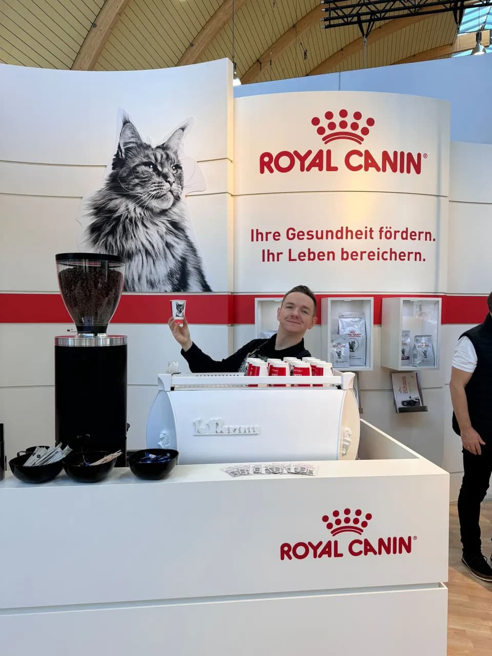Barista an einem Messestand mit großflächigem Kundenbranding im Hintergrund