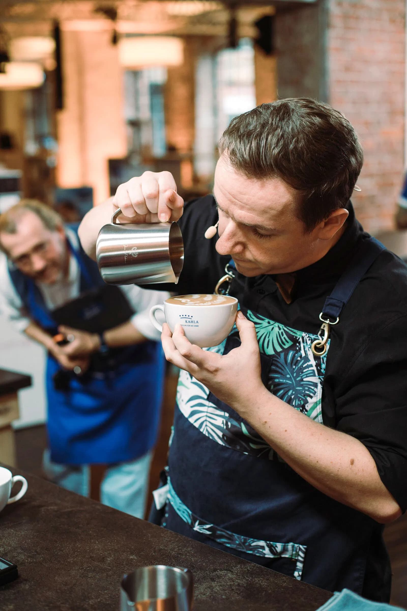 Kai gießt an der Bar Latte Art, die fertige Rosette ist in der Tasse zu sehen